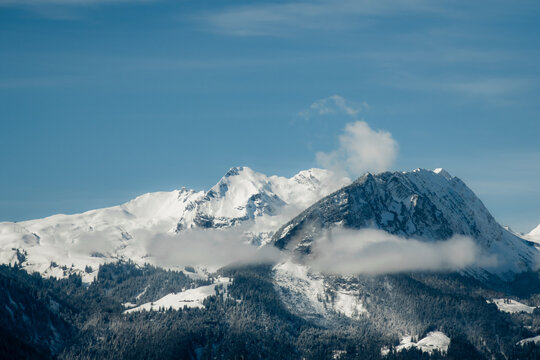 View of snow-capped peaks pierce the azure sky, their majestic forms softened by wisps of ethereal clouds, a winter's tale unfolds, Train from Lucerne, Switzerland.