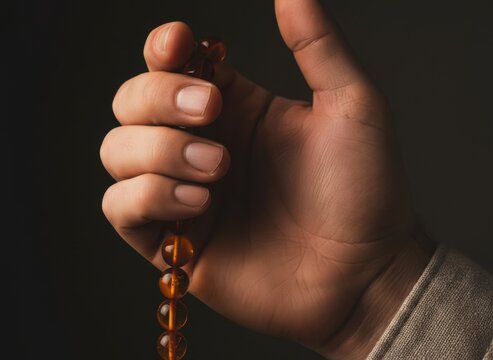 Amber Tasbih Prayer Beads Held in Hand during Meditation with Warm Side Lighting and Dark Background for Spiritual Wellness and Contemplative Religious Practice with Copy Space