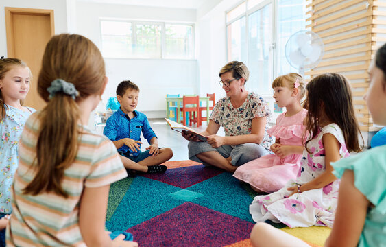 Preschool teacher reading aloud to a group of children during circle time on a colorful rug