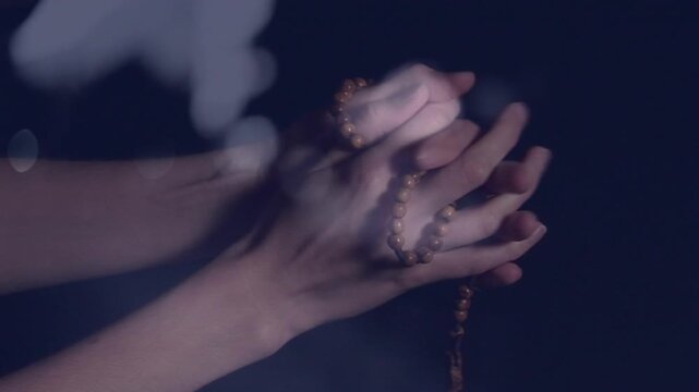 Hands loosening grip and sliding meditation beads with double-exposure bokeh, counting for wellness