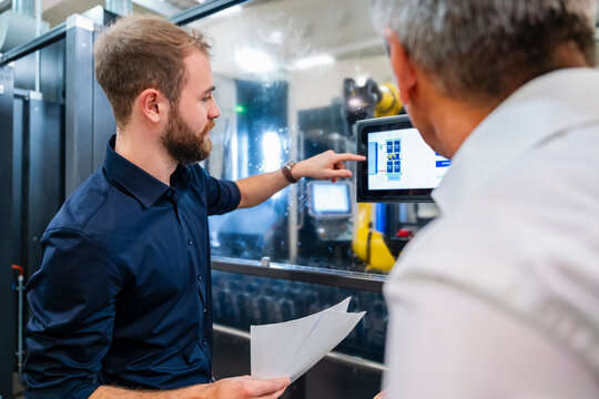 Two men discussing in a production hall with industrial machinery