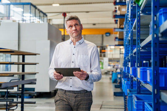 Thoughtful manager with tablet in production hall in industrial setting