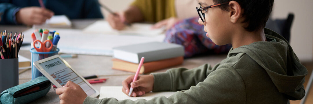 Boy studying at desk with tablet in classroom setting