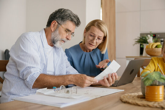 Senior couple reviewing bills with child doing homework nearby