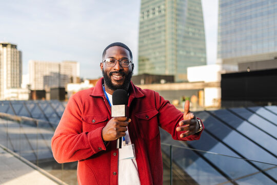 Journalist with microphone presenting on urban rooftop outdoors