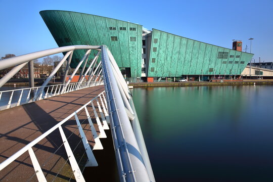 AMSTERDAM, NETHERLANDS - MARCH 04, 2026: The Nemo Science Museum  located in Oosterdok neighborhood, with a modern bridge called Veldebrug in the foreground