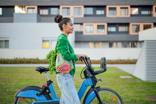 Woman with groceries walking electric bike outdoors in urban area