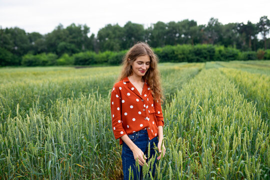 Smiling woman with curly hair in red blouse outdoors in wheat field