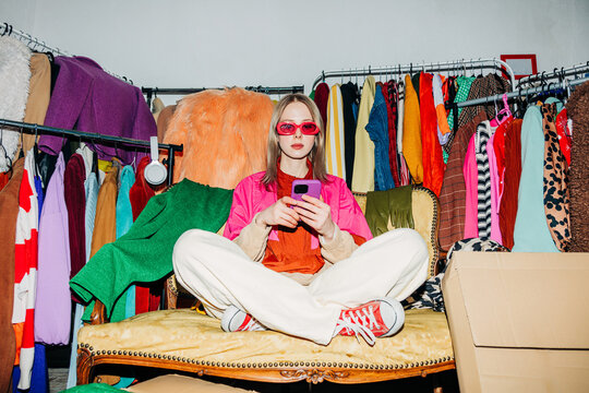 Reseller in colorful wardrobe using smartphone for online clothing sale