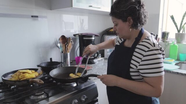 Hispanic woman in apron turning frying plantains in a pan