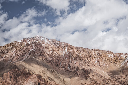 Rocky mountain range with snow and glaciers against a cloudy sky, in the Tien Shan Mountains on Pamirs, stone mountain with red texture, minimalist landscape for background