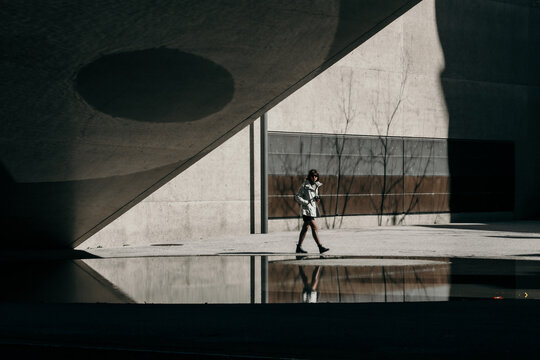 Zurich, Switzerland - 02 April 2023: View of a solitary figure strides past the National Museum, its stark concrete contrasting with the water reflection.
