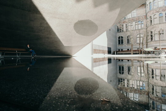 Zurich, Switzerland - 02 April 2023: View of the National Museum's architecture reflected in a still puddle, where light and shadow dance on the concrete, creating a mesmerizing contrast.