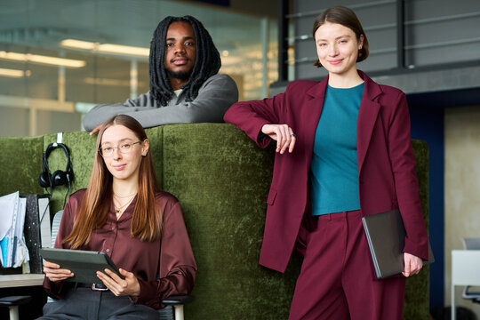 Portrait of diverse young coworkers posing with tablet and laptop in office, representing teamwork and workplace culture. Ideal for recruitment, corporate branding, team pages