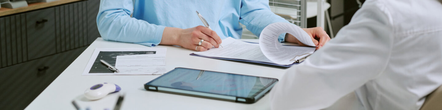 Website banner of patient signing medical documents during consultation with doctor at desk