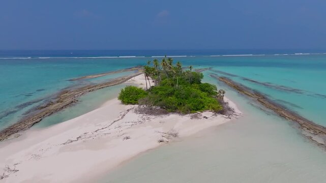 Aerial drone flight over a rocky tropical islet in the Maldives surrounded by turquoise lagoon and clear ocean with natural rugged island scenery