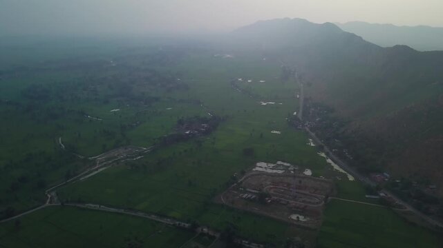 High-angle view over rural agricultural valley with green fields, scattered settlements, and mountain ridges under hazy dawn light in Jethian Range, Firojpur district, Bihar, India.