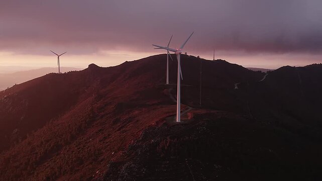 Horizontal axis 3 blade up wind turbines on Serra da Boneca in Penafiel Porto District Norte Portugal installed along exposed ridge with service road across rocky terrain under warm sunset light