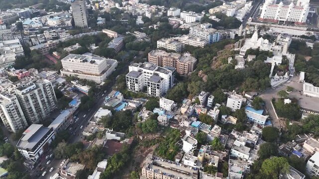 Cinematic aerial view of Hyderabad showcasing dense residential blocks, tree-lined streets, and mid-rise buildings surrounding the hilltop Birla Mandir, blending greenery with structured urban develop