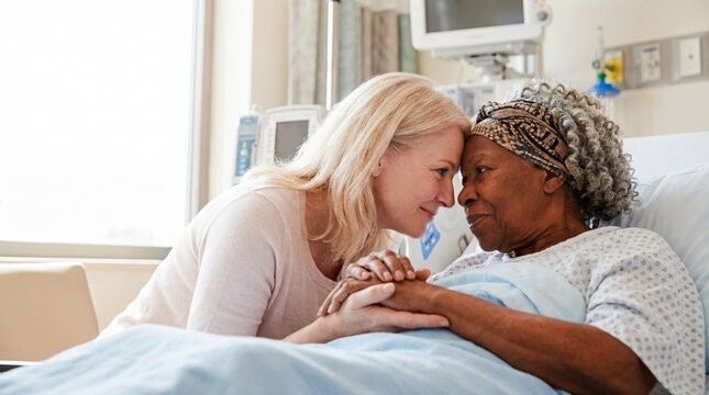 white woman comforting elderly Black patient in hospital with tenderness through handholding and forehead touch to express family love emotional support recovery hope and caregiving