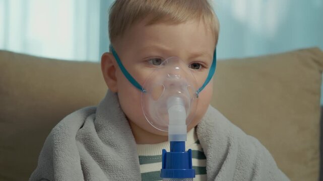 A child is receiving treatment with a nebulizer mask to help with cough and respiratory infection at home. The child breathes in the saline solution for relief.