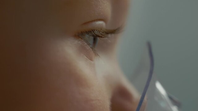 A close up shows a child inhaling medication through a mask to treat cough and respiratory issues at home. The treatment focuses on easing breathing difficulties.