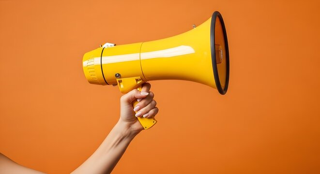 Hand holding bright yellow megaphone bullhorn for announcement and marketing campaign on vibrant orange background