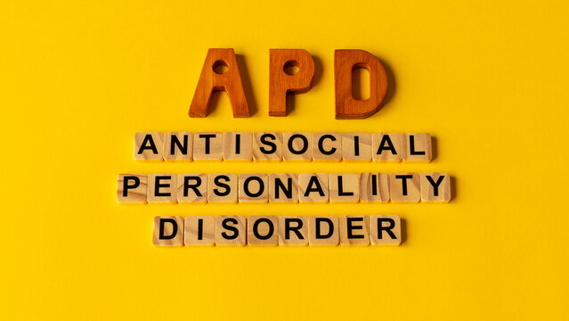 APD abbreviation on wooden letters and its individual words: Antisocial Personality Disorder, spelled out with wooden letter tiles on a vivid yellow background.