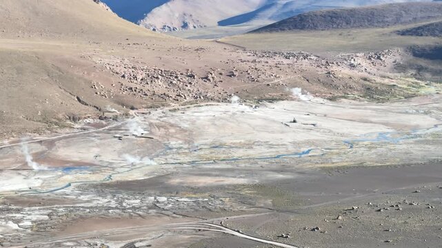 Cinematic aerial moving forward over steaming geothermal vents of El Tatio at dawn, revealing the volcanic landscape of the Chilean Altiplano