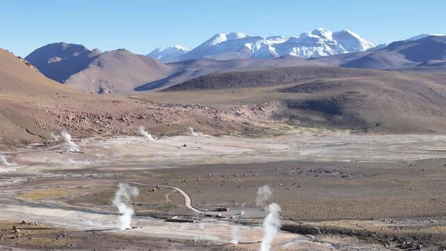 Cinematic aerial pulling back from steaming geothermal vents to reveal the vast El Tatio geyser field nestled among the volcanic peaks of the Chilean Altiplano