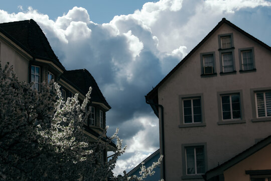 Zurich, Switzerland - 02 April 2023: View of traditional architecture meeting a vibrant sky, where the stark white buildings are juxtaposed against the billowing storm clouds.