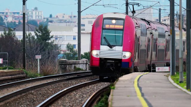 Front view of red electric train approaching station on cloudy day, urban background, motion.
