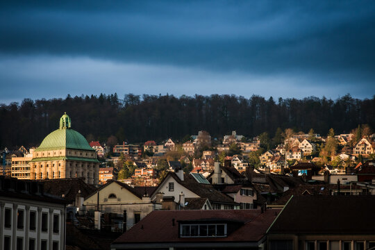 Zurich, Switzerland - 02 April 2023: View of the Urania Sternwarte's green dome contrasting against the rooftops and dark forest, bathed in the warm glow of the setting sun.