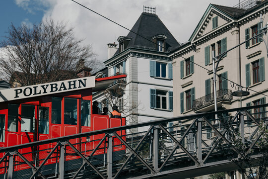 Zurich, Switzerland - 02 April 2023: View of the bright red Polybahn funicular ascending through the city against a backdrop of elegant buildings and a partly cloudy sky.