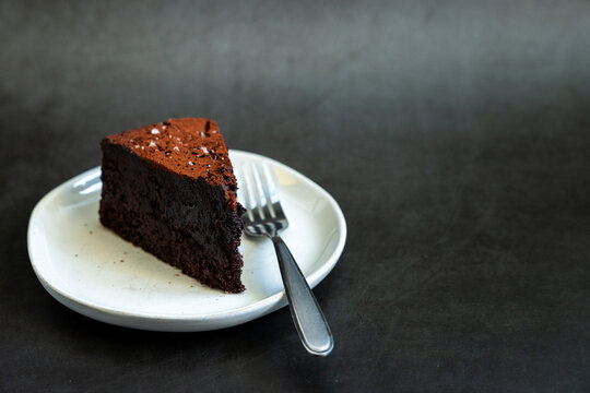 Flourless chocolate cake sprinkled with salt on a white plate with dark backdrop