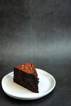 Flourless chocolate cake sprinkled with salt on a white plate with dark backdrop