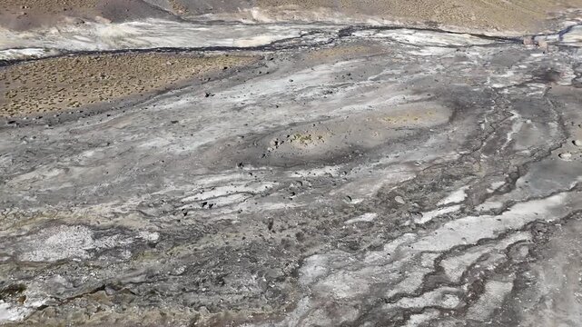 Cinematic aerial flying forward toward a steaming, emerald-green geothermal pool surrounded by mineral deposits at El Tatio Geyser Field, Chile