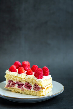 Yellow cake with raspberries and cream on a plate with a dark backdrop
