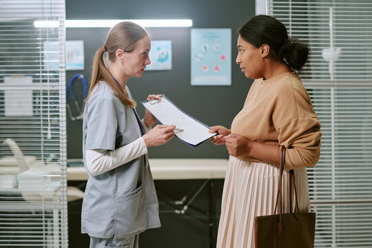 Medium shot of Caucasian female doctor consulting pregnant woman, reviewing medical form during prenatal visit