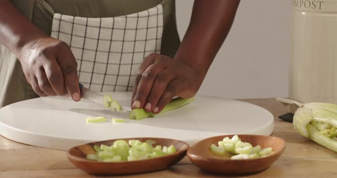 African man positioning stalk, slicing with chef knife on cutting board, prepping meal by compost