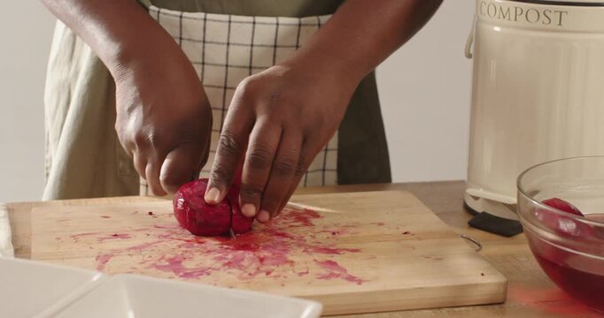 African American man dicing red beet using paring knife on kitchen counter wearing light apron