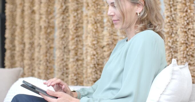 Closeup pulling back while woman wearing lav mic for recording tapping tablet on sofa smiling