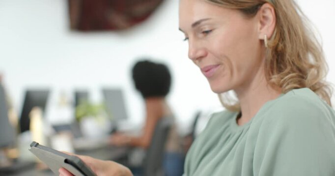 Middle-aged woman during pullback holding tablet and scrolling to review work in office, copy space