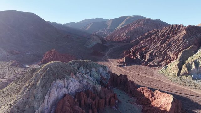 Cinematic aerial flying sideways to the right over a multi-colored mineral peak to reveal the expansive red rock canyons and winding desert tracks of Valle del Arcoiris (Rainbow Valley) near San Pedro