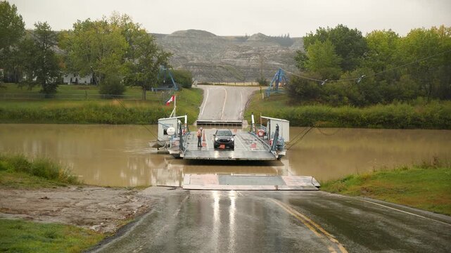 Car ferry boat crossing a red deer river with vehicle and passengers during a rainy day in Drumheller, Alberta Canada Jurassic Looking Dinosaur Country. High quality 4k footage