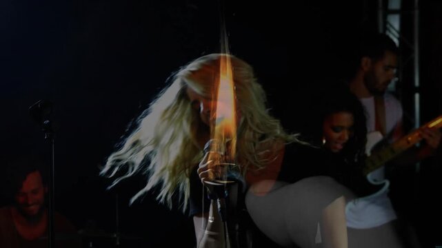 Lead singer singing on dim stage, causing flame projecting over microphone, band playing music