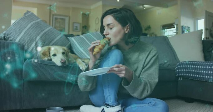 Woman on rug lifting croissant showing teal overlays, eating, petting dog, reaching mug for snack