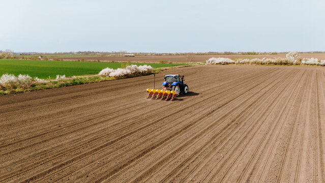 Aerial view of a vibrant blue tractor cutting through the rich brown earth, preparing the fields for planting, Sremska Mitrovica, Vojvodina, Serbia.