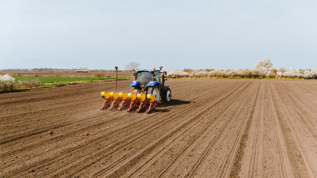 Aerial view of a blue tractor meticulously planting seeds in neat rows across the rich, brown earth of a vast field, Sremska Mitrovica, Vojvodina, Serbia.