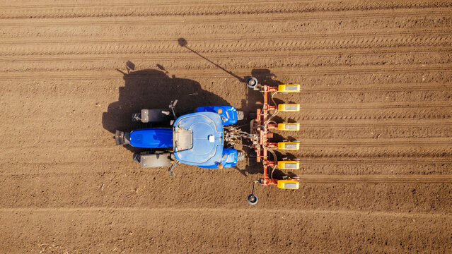 Aerial view of a bright blue tractor with orange implements contrasts against the rich brown earth of a freshly plowed field, Sremska Mitrovica, Vojvodina, Serbia.